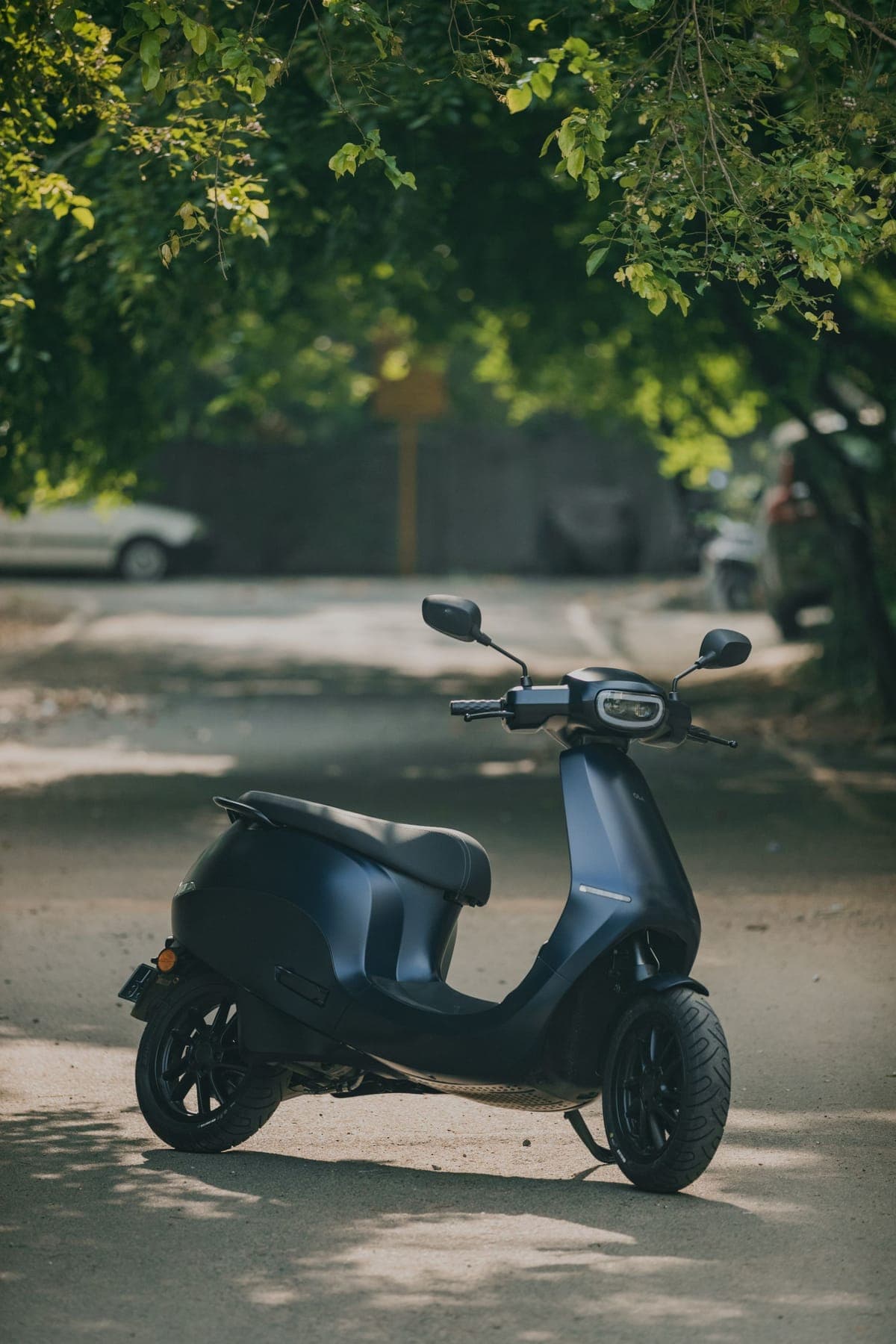 An electric scooter parked on a tree-lined road
