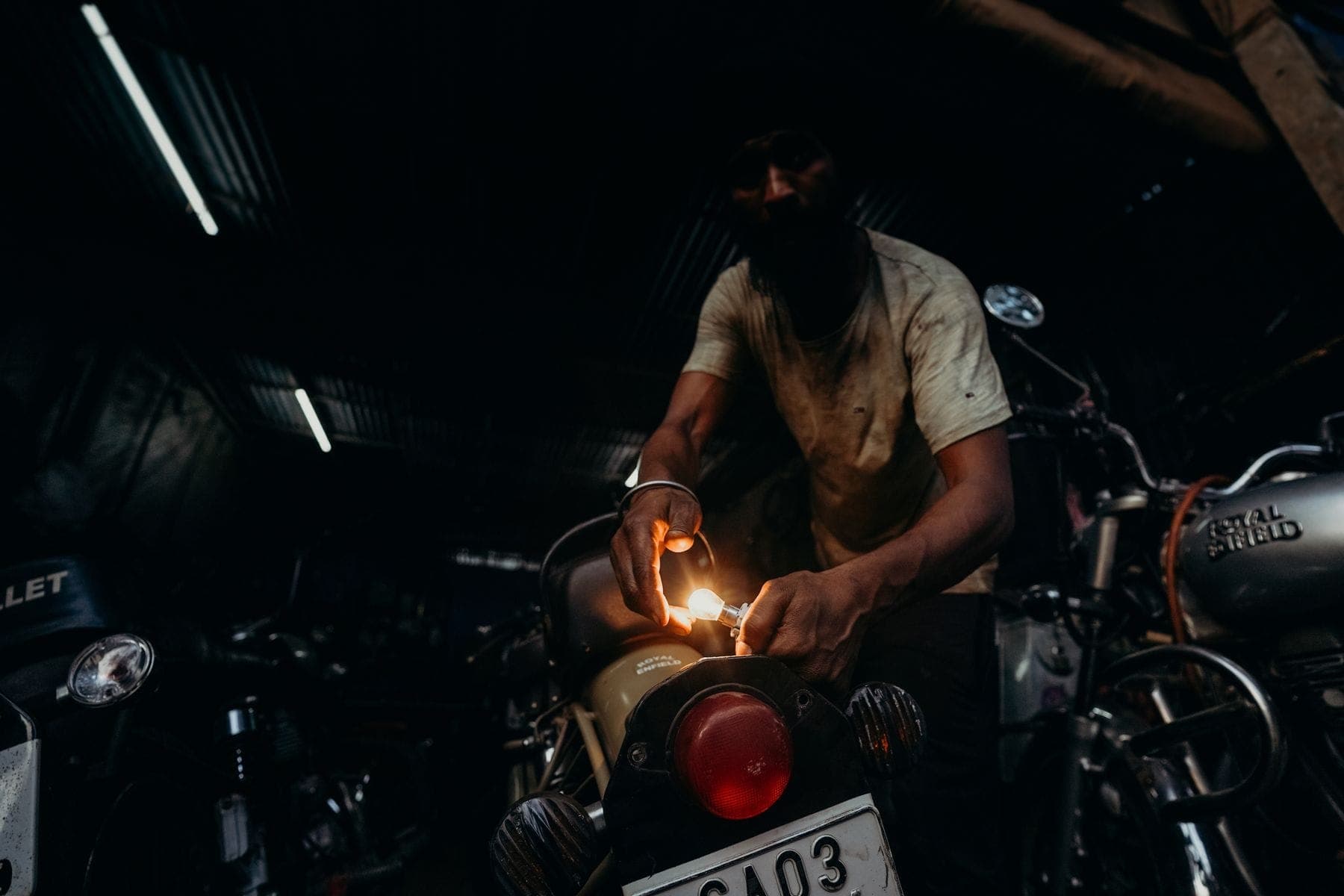 A mechanic working on a two-wheeler under a work lamp