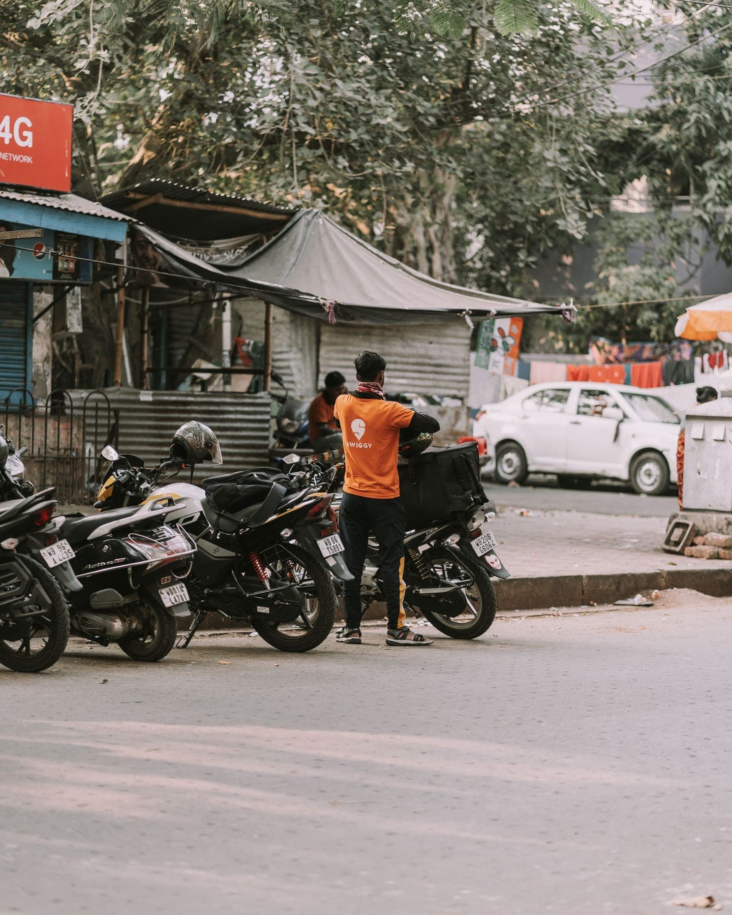 A delivery rider with an insulated backpack beside parked two-wheelers