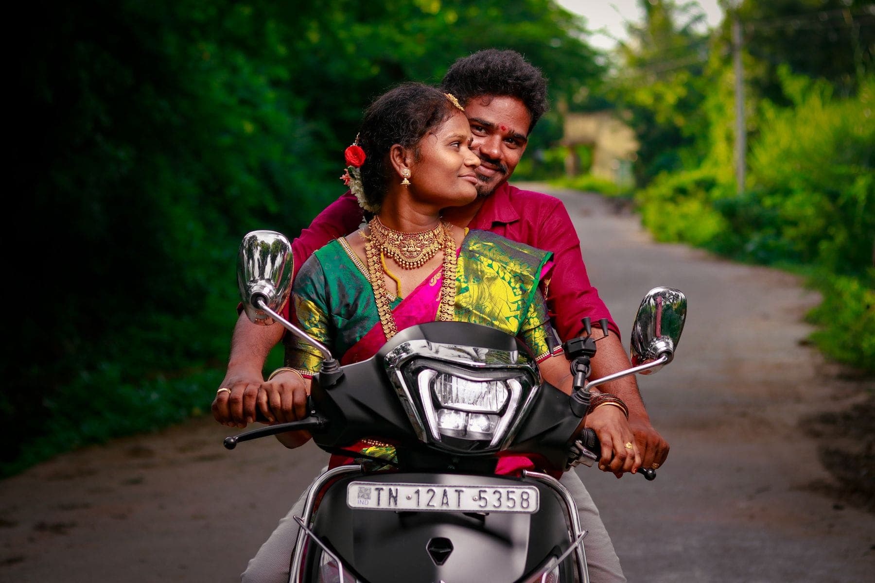 Two people riding a scooter together on a green country road